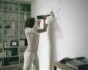 woman tries to hang a picture on wall by herself.