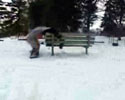 a kid jumps on snowboard over bench.